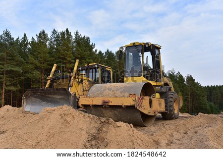Dozer and Vibro Roller Soil Compactor at road construction and bridge projects in forest area. Heavy machinery for road work. Building a road works. 