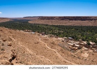 Draa Valley, high angle view of the lush green palm oasis of the Ziz Valley nestled between arid rocky cliffs with a traditional village in the High Atlas region of Morocco