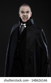 Dracula With Black Cape Showing His Scary Teeth. Vamp Fangs. Studio Shot Against Black.