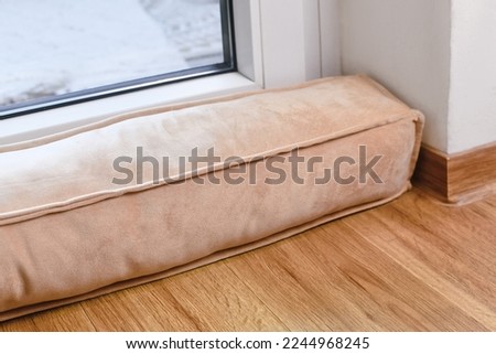 Draft excluder lying in front of door to keep out cold air and save energy for heating in room