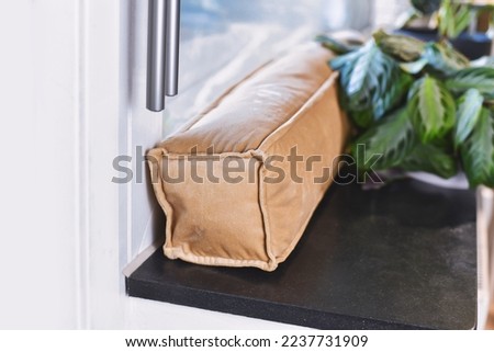 Draft excluder lying on window still to keep out cold air and save energy for heating in room