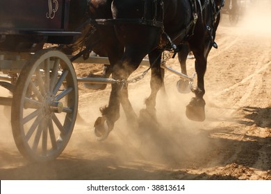 Draft Horses Pulling A Wagon Through A Dusty Field.