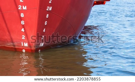 Draft mark numbers on red Hull surface of metal Ship while docked at shipyard area for renovate work