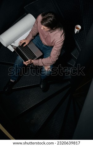 Drafter using his portable computer on spiral staircase in building