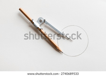 Drafting compass drawing circle on white paper background top view. 