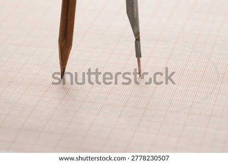 Drafting compass drawing circle on graph millimeter paper background closeup, architect's tool. 