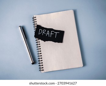 Drafting a Document Concept: Notebook, Silver Pen, and Black Paper with White 'Draft' Text for Writing and Revision