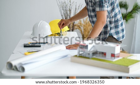 Draftsman is designing house plan, model houses and house plans with a safety helmet on the desk.
