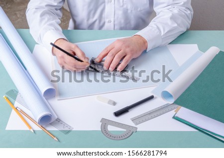 Draftsman using t-square and pencil for drafting on the graph paper. Professional constructor`s workplace