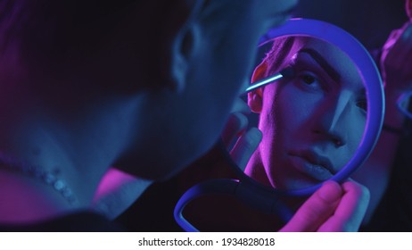 Drag artist - young man applying base color on his eyes - blue and purple neon lighting