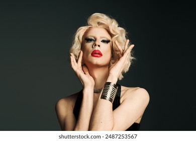 A drag queen with bold makeup and a blonde wig poses in a black dress against a grey backdrop. - Powered by Shutterstock