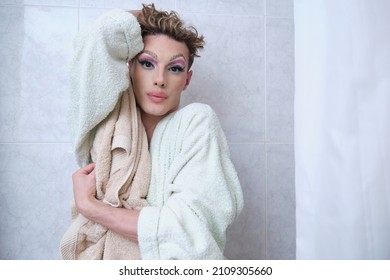 Drag Queen Person Wearing Bathrobe Posing Looking At Camera In A Bathroom.