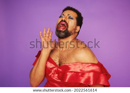 Drag queen singing in a theater. Man with beard wearing makeup and female dress giving a theatrical performance.