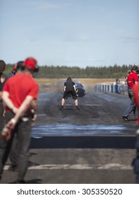 A Drag Race Car Heading Up For Top Speed In The Drag Race Weekend On A Hot Summer Day. A Team Members Are Watching Behind The Race Strip.