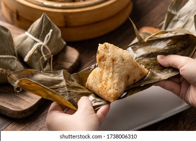 Dragon Boat Festival food - Rice dumpling zongzi, young Asian woman eating Chinese traditional food on wooden table at home celebration, close up