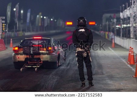 Dragster driver with drag car in race track at night, Drag racing car at the start competition at night, Drag race car in race track at night, Sport car at the start, speed competition.
