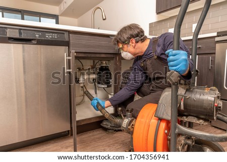 Drain cleaning by professional plumber wearing a safety mask, using an auger
