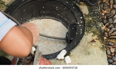 Drain cleaning. Plumber repairing clogged grease trap with auger machine. Maintenance the sewage system and grease trap by professional plumber. Using auger snake to fix and unclog a drain. - Shutterstock ID 2054593718
