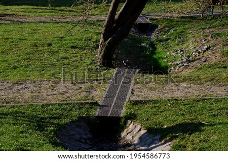 Drainage of the path by means of a gutter under which water flows. the gutter is covered with a metal grid. grassy area with paths on the slope 