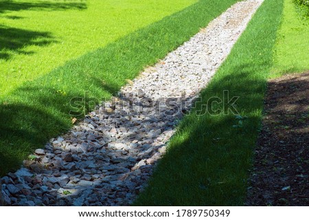 drainage, a drainage system in a Park area, a waterway overgrown with lawn and paved with stones, an Aqueduct between nature and the road. stone water drains in a grass garden field. Lawn and plant