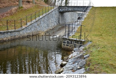 drainage of drainage water from the bottom of the dam dam or pond through the upper safety overflow water overflow determines the maximum level. lake level with stone paneling and metal railings.