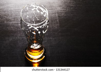 drained glass of fresh lager beer on black table