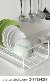 Drainer with different clean dishware on light table in kitchen