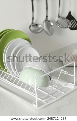 Drainer with different clean dishware on light table in kitchen