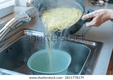 Draining freshly cooked spaghetti into a colander with steaming pasta and flowing hot water in a kitchen sink
