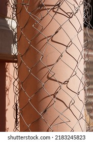 Drainpipe Wrapped In Steel Mesh With Square Cells. Interlacing Of Metal Wire. Abstract Grunge Background With Shadows. Focus On Foreground. Vertical Photo.

