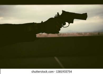 Drama And Cinematic 70s Shot Of A Silhouette Of A Man Wearing A Jacket And Bracelet While Holding A Gun And Aiming It At Someone Off Screen In A Parking Garage