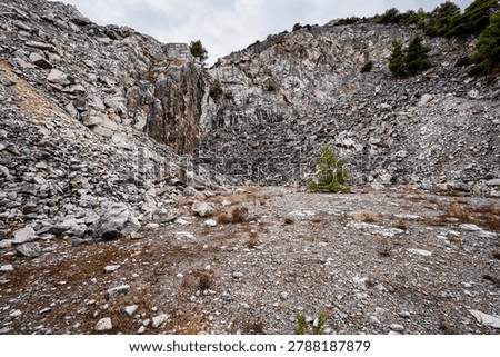 Dramatic abandoned marble quarry on Penteli Mountain near Athens, Greece, featuring rugged rock walls, scattered stone debris and sparse Mediterranean vegetation.