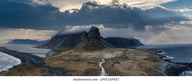 Dramatic aerial landscape of Iceland featuring a winding road through a misty valley, volcanic beach, and majestic mountain range shrouded in clouds. - Powered by Shutterstock