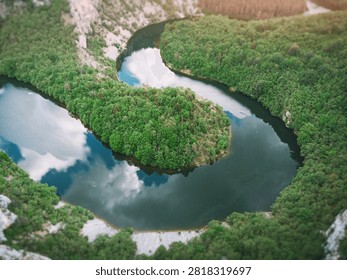 Dramatic aerial perspective of a double river meander forming an S-curve through dense forested canyon with limestone cliffs and calm reflective water.