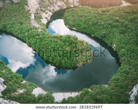 Dramatic aerial perspective of a double river meander forming an S-curve through dense forested canyon with limestone cliffs and calm reflective water.