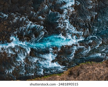 Dramatic aerial view of a bright blue river flowing through dark, rocky banks in Iceland. The water churns and froths, creating a stunning natural scene. - Powered by Shutterstock