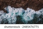 A dramatic aerial view capturing the raw power of ocean waves as they crash against a rugged rocky cliff, showcasing the beauty and strength of nature.