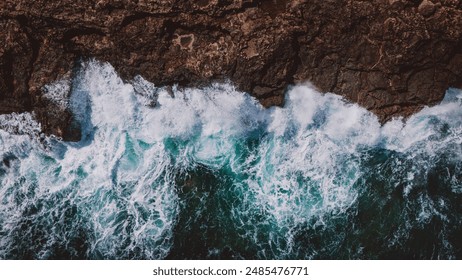 A dramatic aerial view capturing the raw power of ocean waves as they crash against a rugged rocky cliff, showcasing the beauty and strength of nature. - Powered by Shutterstock