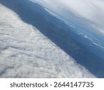 Dramatic aerial view of dense cloud formations drifting over tropical mountain ranges in Indonesia. High altitude scene showing cloud front and rugged terrain.