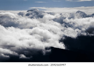 Dramatic aerial view of dense clouds covering mountain peaks, creating a mystical and surreal atmosphere. The contrast of light and shadow enhances the depth of the sky and landscape. Ideal for travel