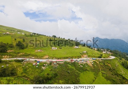 A dramatic aerial view of the mountain landscape in Flesha, Ainaro, Timor-Leste. A winding road passes through a remote village nestled among lush green hills.