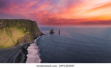 Dramatic aerial view of a rugged cliff and black sand beach in Iceland at sunset. Vibrant sky colors and distant sea stacks create a breathtaking coastal scene. - Powered by Shutterstock