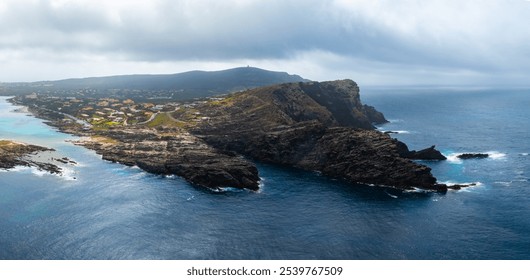 Dramatic aerial view of Sardinia's coastline featuring rocky cliffs, small settlements, and a hill with a structure under overcast skies. - Powered by Shutterstock