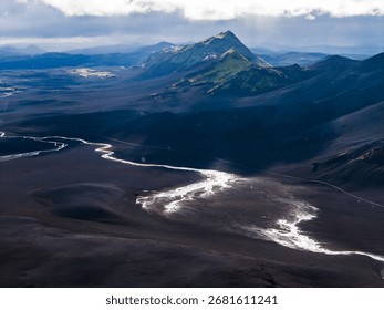Dramatic aerial view of a sharp peaked mountain in Iceland, surrounded by dark volcanic plains, a winding river, and distant mountain ranges.