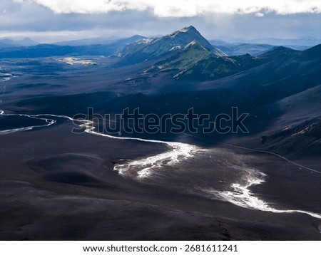 Dramatic aerial view of a sharp peaked mountain in Iceland, surrounded by dark volcanic plains, a winding river, and distant mountain ranges.