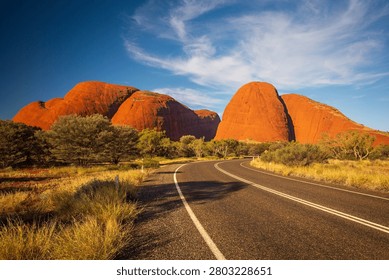Dramatic afternoon light falls over road curving into Kata Tjuta (The Olgas) landform in Central Australia. 