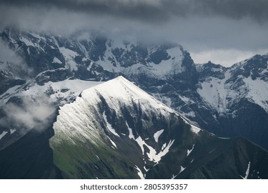 A dramatic alpine landscape featuring a rugged, snow-covered mountain ridge under a moody sky. The sharp crest of the mountain extends diagonally through the frame, with steep rocky slopes partially covered in fresh snow. Thick clouds drift across the peaks, obscuring parts of the background mountains and creating an atmosphere of mystery and grandeur. The contrast between the dark rock faces, bright white snowfields, and stormy gray clouds emphasizes the harsh beauty of the high-altitude environment. The image conveys a sense of isolation, power, and the untamed nature of the alpine wilderness.
Taken in the Allgäuer Alps near the Nebelhorn summit with the view towards south-east