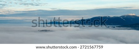 Dramatic alpine landscape over Burnaby and Greater Vancouver, BC, Canada, with a soft sea of clouds and snow-capped peaks.