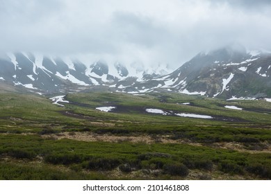 Dramatic alpine landscape with snowy mountains in gray low clouds. Bleak atmospheric scenery of tundra under lead gray sky. Gloomy minimalist view to mountain range among low rainy clouds in overcast. - Shutterstock ID 2101461808