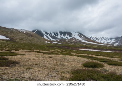 Dramatic alpine landscape with snowy mountains in gray low clouds. Bleak atmospheric scenery of tundra under lead gray sky. Gloomy minimalist view to mountain range among low rainy clouds in overcast. - Shutterstock ID 2106271430